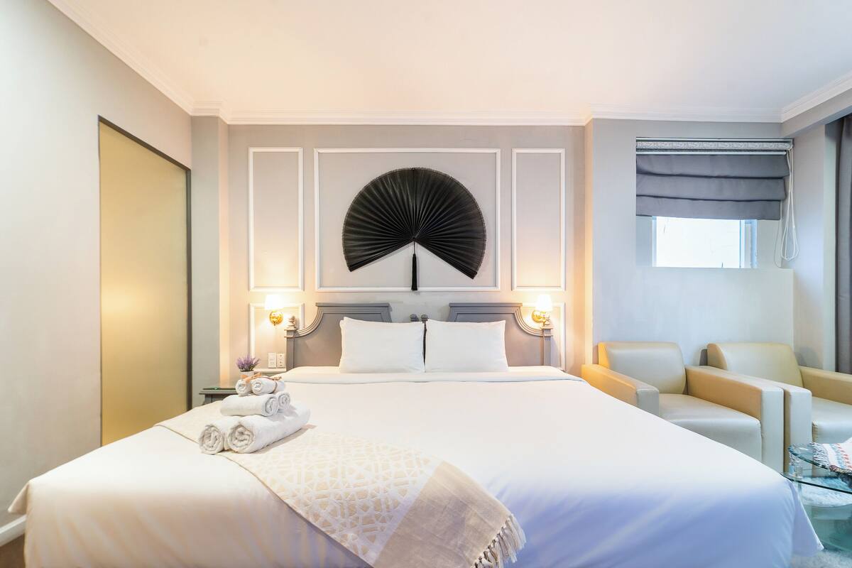 Ein Hotelzimmer mit einem großen Bett, zwei Nachttischen mit Lampen, einem Sessel und einem Fenster mit Vorhängen.
