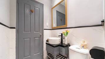 A bathroom with a grey door, a white sink with a black countertop, a mirror with a gold frame, and a toilet with a black lid.