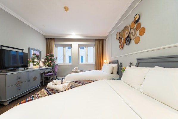 Quarto de hotel com duas camas, uma mesa com computador, televisão e um painel decorativo na parede.
