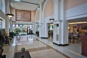 Een ruime lobby met hoge plafonds, grote ramen en een centrale zithoek.