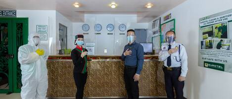 A hotel reception area with a green door labeled "EL ENTRANCE," a sign prohibiting minors, and a poster about room cleaning and sanitization.