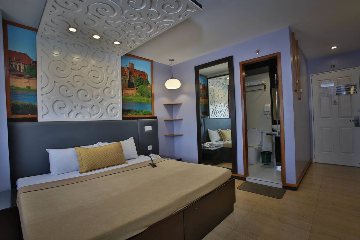 A modern hotel room with a large bed, a bathroom with a mirror, and a painting on the wall.