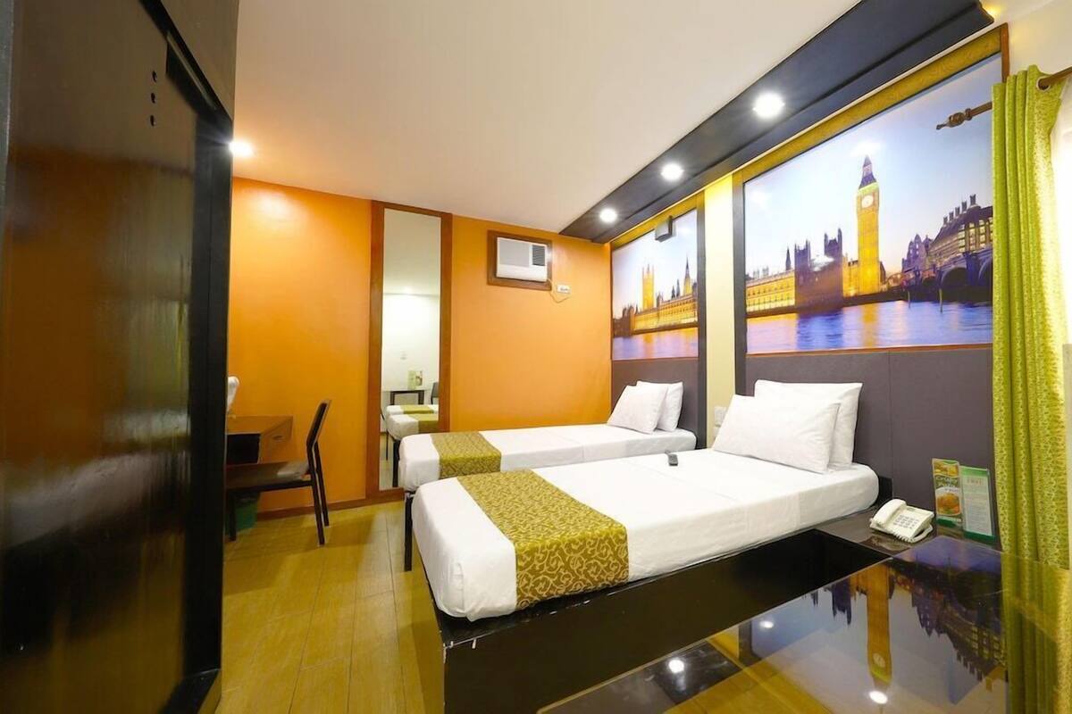 A hotel room with two beds, a desk, a chair, a mirror, and a large window with a cityscape view.