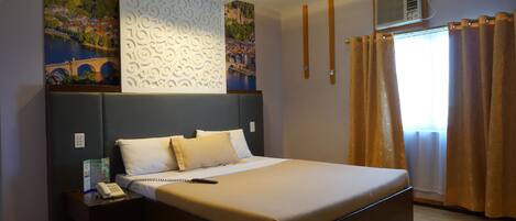 A neatly arranged hotel room with a large bed, a bedside table with a phone, and a wall with a scenic painting.