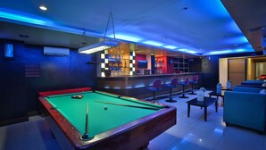 Une table de billard recouverte d’un drap vert, un bar avec des tabourets et un coin salon avec des canapés bleus.