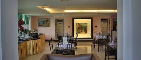 A modern hotel lobby with a brown leather sofa, dining area, and artwork on the walls.
