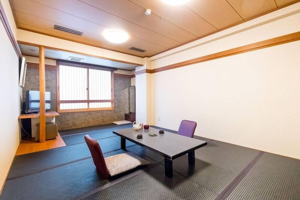 A room with tatami mats, a tatami mat bench, a table with tea ceremony utensils, a television, and a sliding door leading to another room.