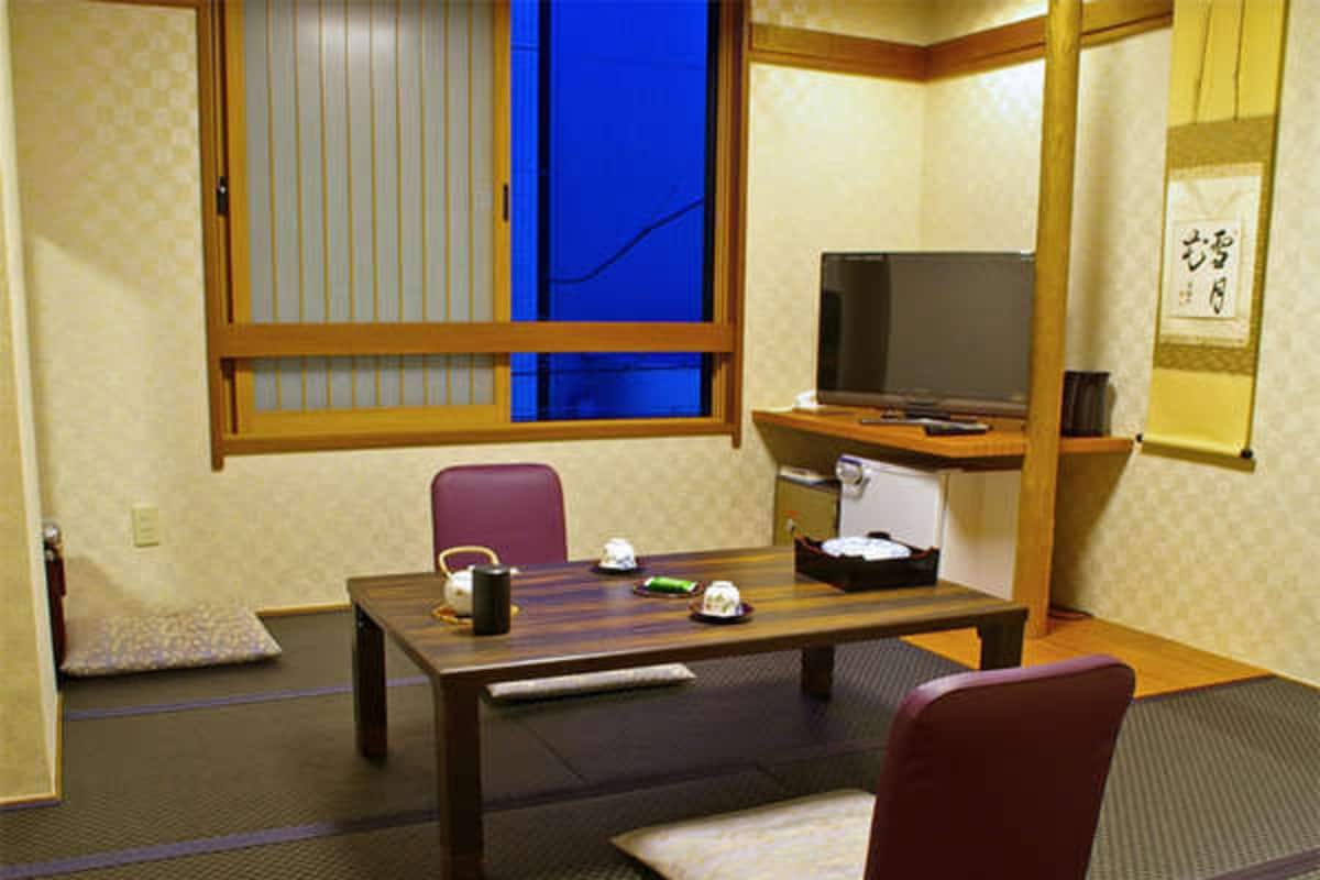A traditional Japanese room with tatami flooring, a low table, a television, and a futon bed.