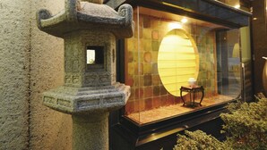 Un farol de piedra con un ventanal pequeño, una vitrina con frente de vidrio y una mesita con una lámpara en su interior.