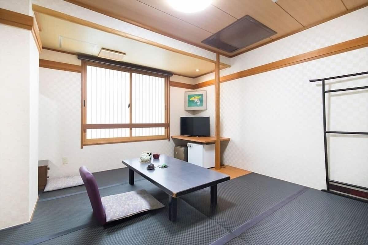 A room with tatami flooring, a low table, a chair, a television on a shelf, and a sliding door.