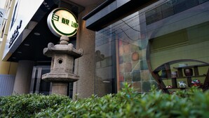 Fachada de edificio con un farol de piedra, escaparate de vidrio y un letrero con caracteres japoneses.