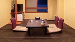 Una habitación tradicional japonesa con suelo de tatami, una mesa baja y dos zonas de estar acolchadas.