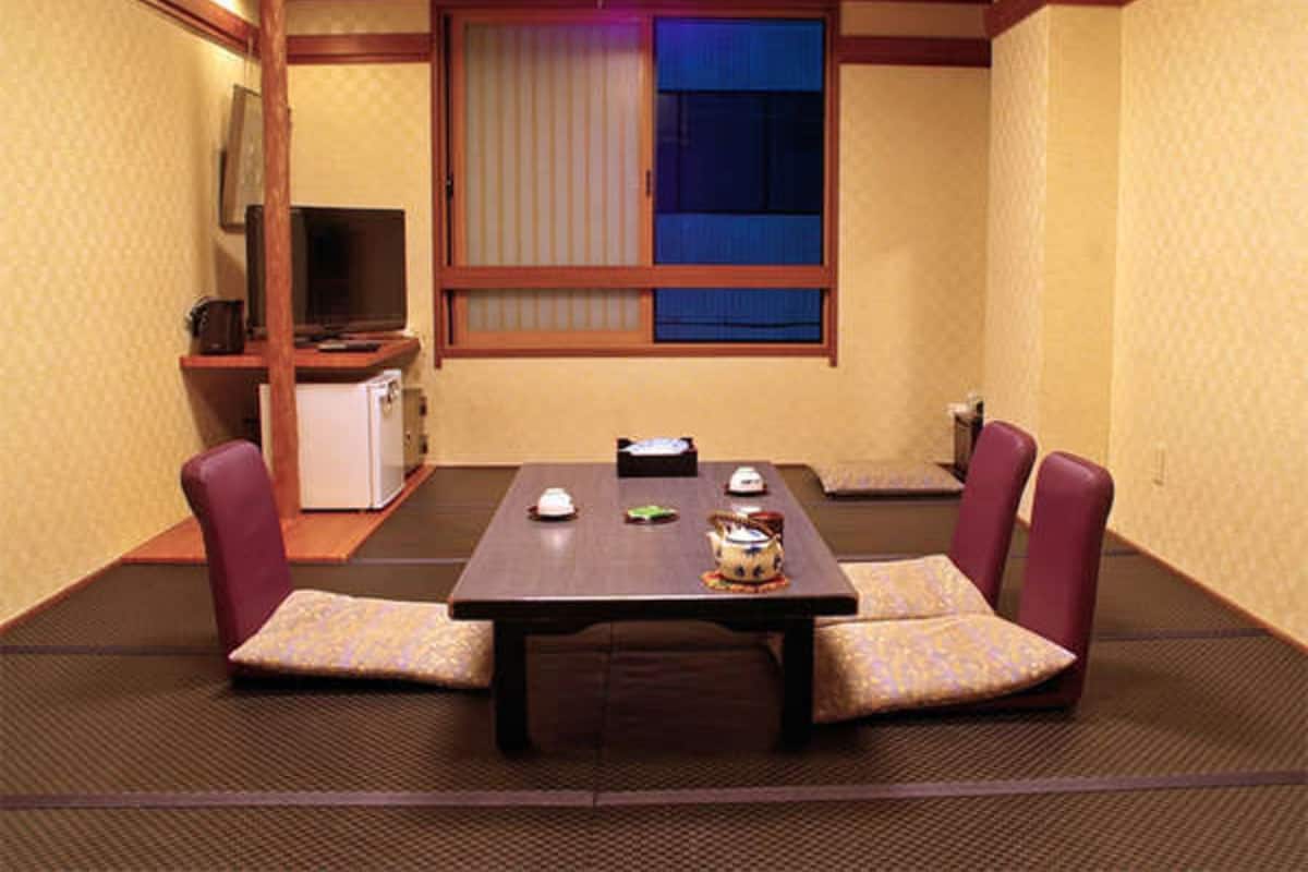 A traditional Japanese room with tatami flooring, a low table, and two cushioned seating areas.