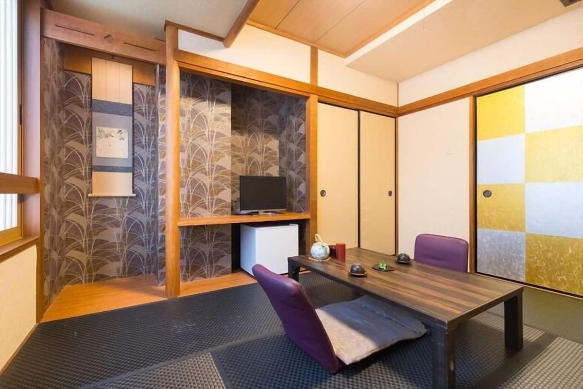 A traditional Japanese-style room with tatami flooring, a low table, a television, and sliding doors.