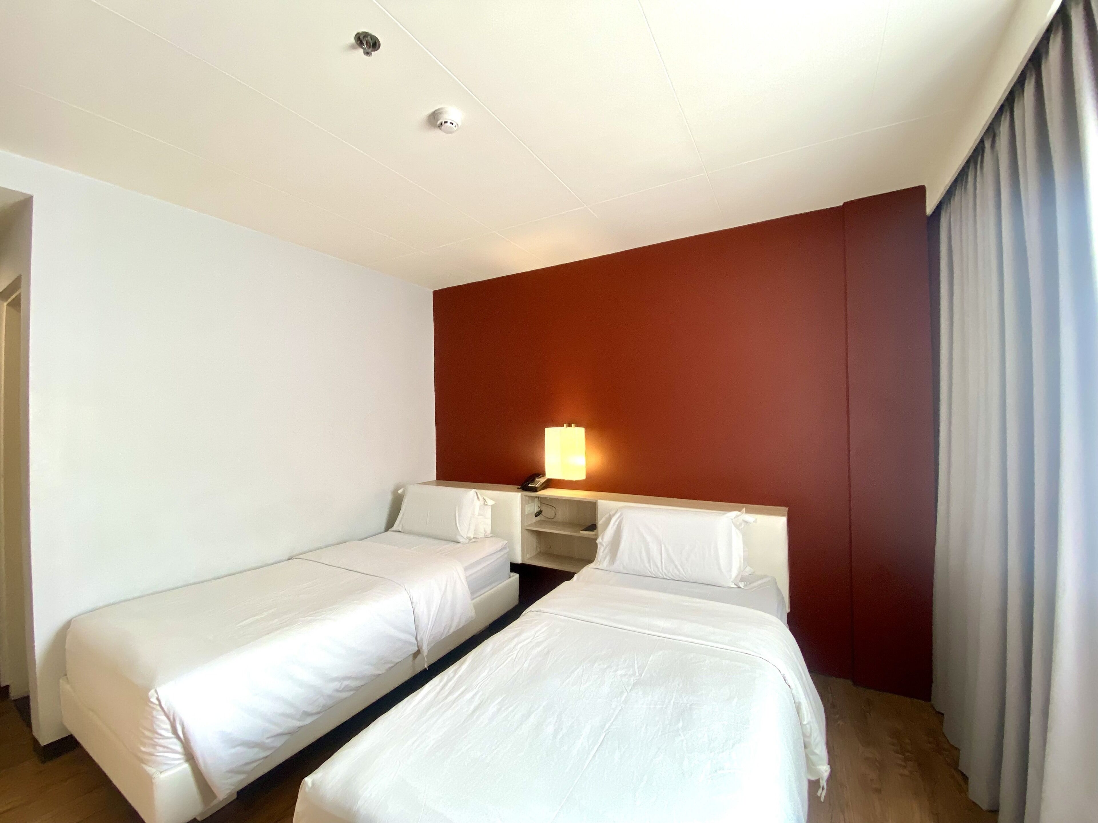 A hotel room with two single beds, a desk with a lamp, and a red accent wall.