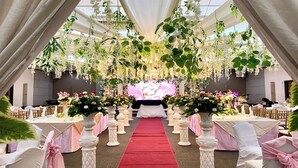 Un salón de bodas con alfombra roja, arreglos florales blancos y follaje colgante.