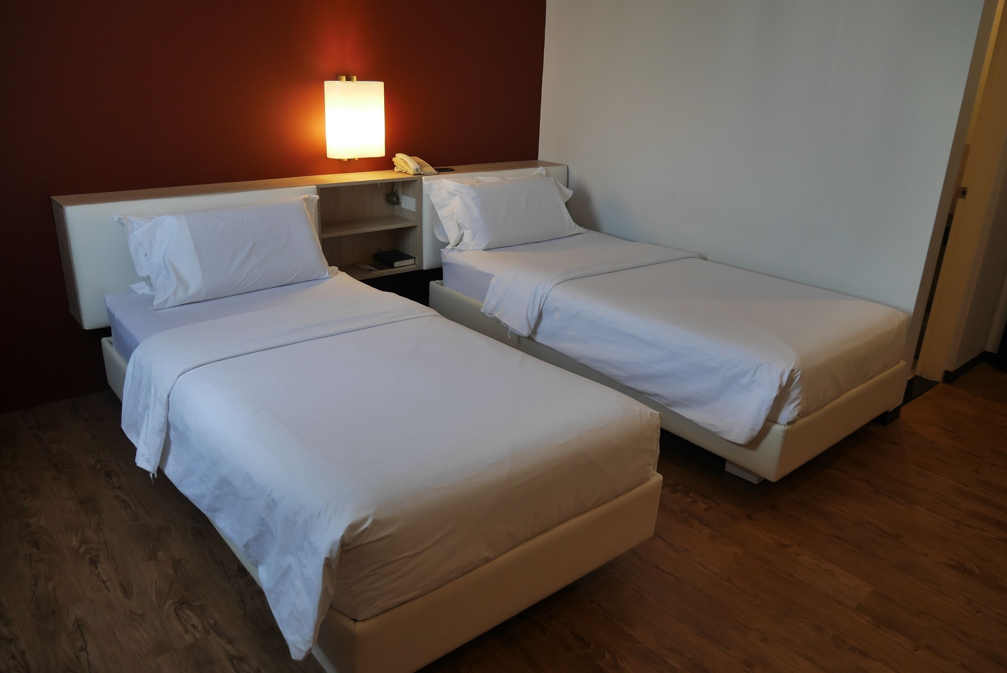 A hotel room with two single beds, a bedside table with a lamp, and a phone.