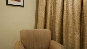 A room with a single armchair, a framed picture on the wall, and patterned curtains.