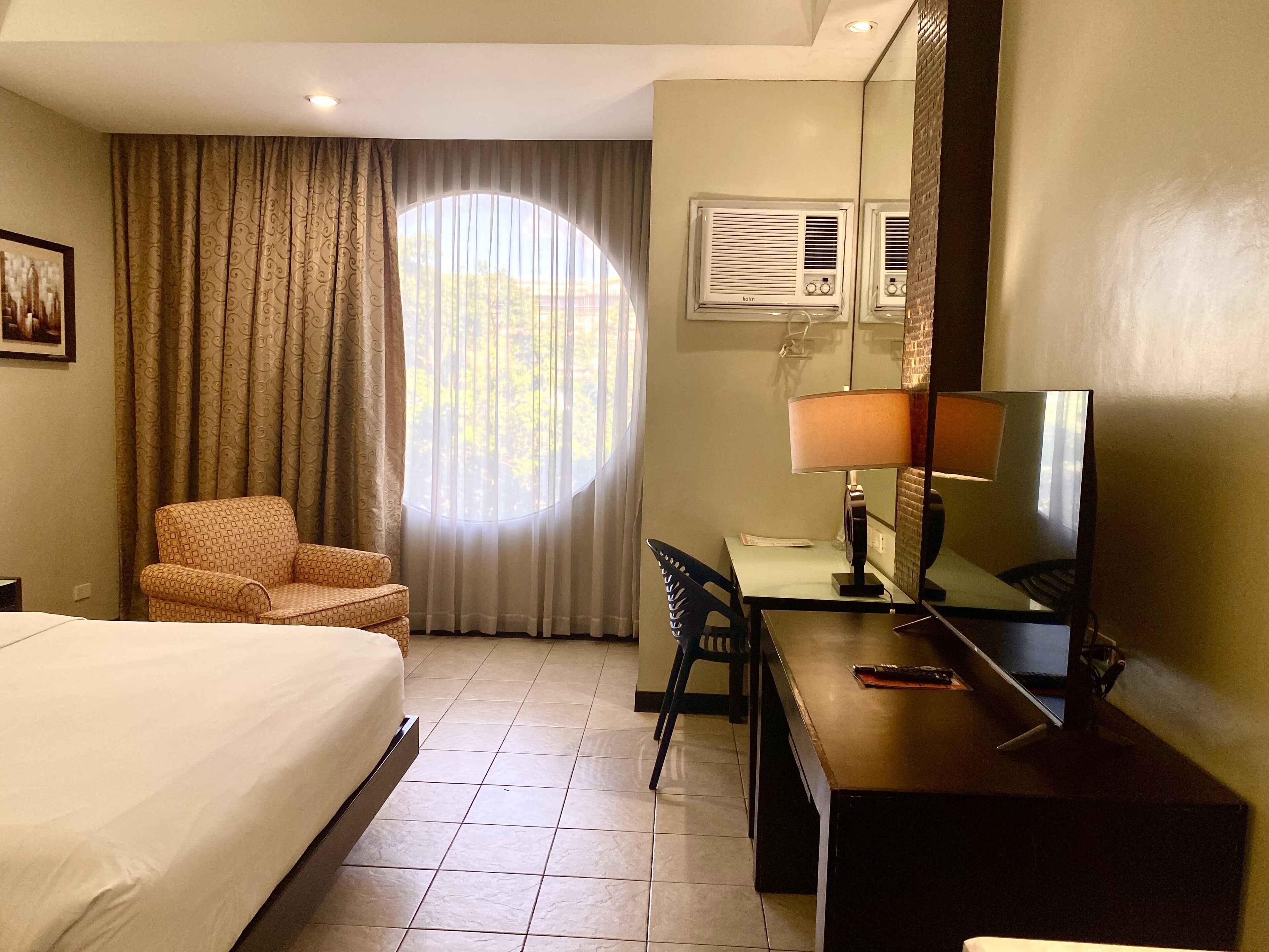 A hotel room with a bed, a desk, a chair, a television, and a window with curtains.