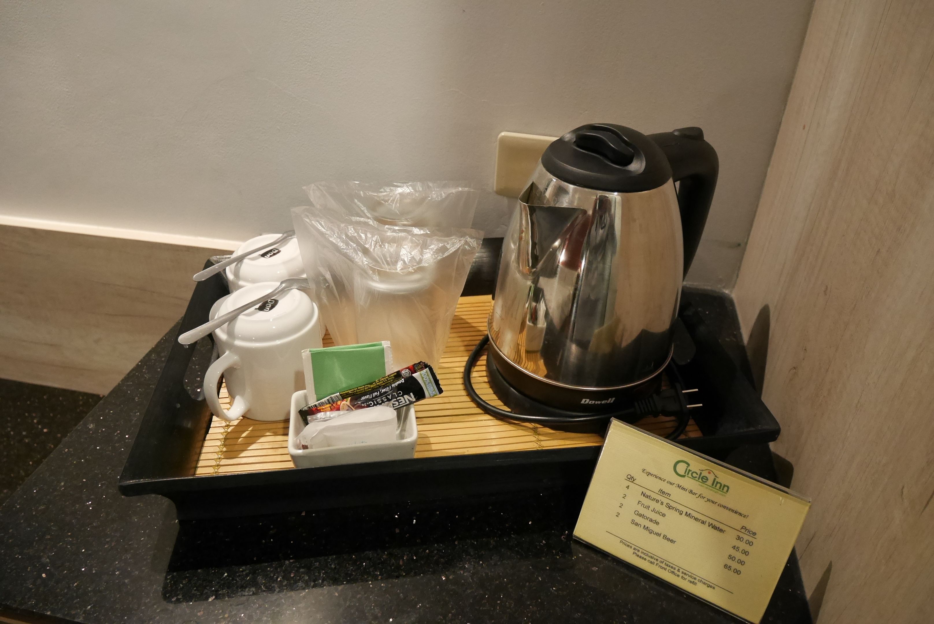 Bandeja de desayuno en una habitación de hotel, con una cafetera, un hervidor de té, una taza, un sobre de azúcar y un dispensador de servilletas.
