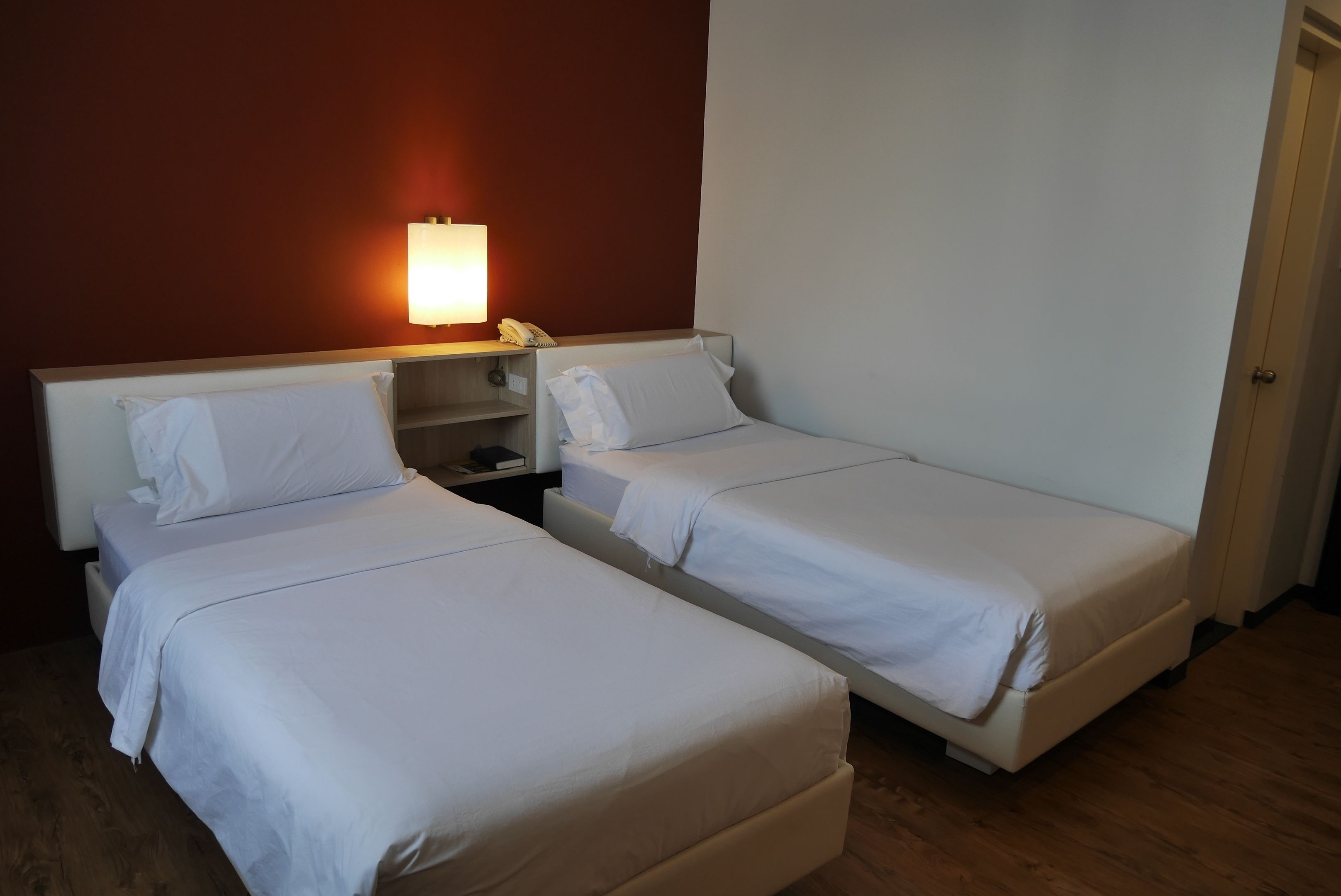 Two single beds with white linens in a room with wooden flooring and a red accent wall.