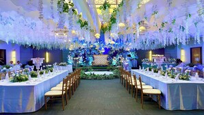Un salón de banquetes con mesas largas, un escenario central y decoraciones florales colgantes.