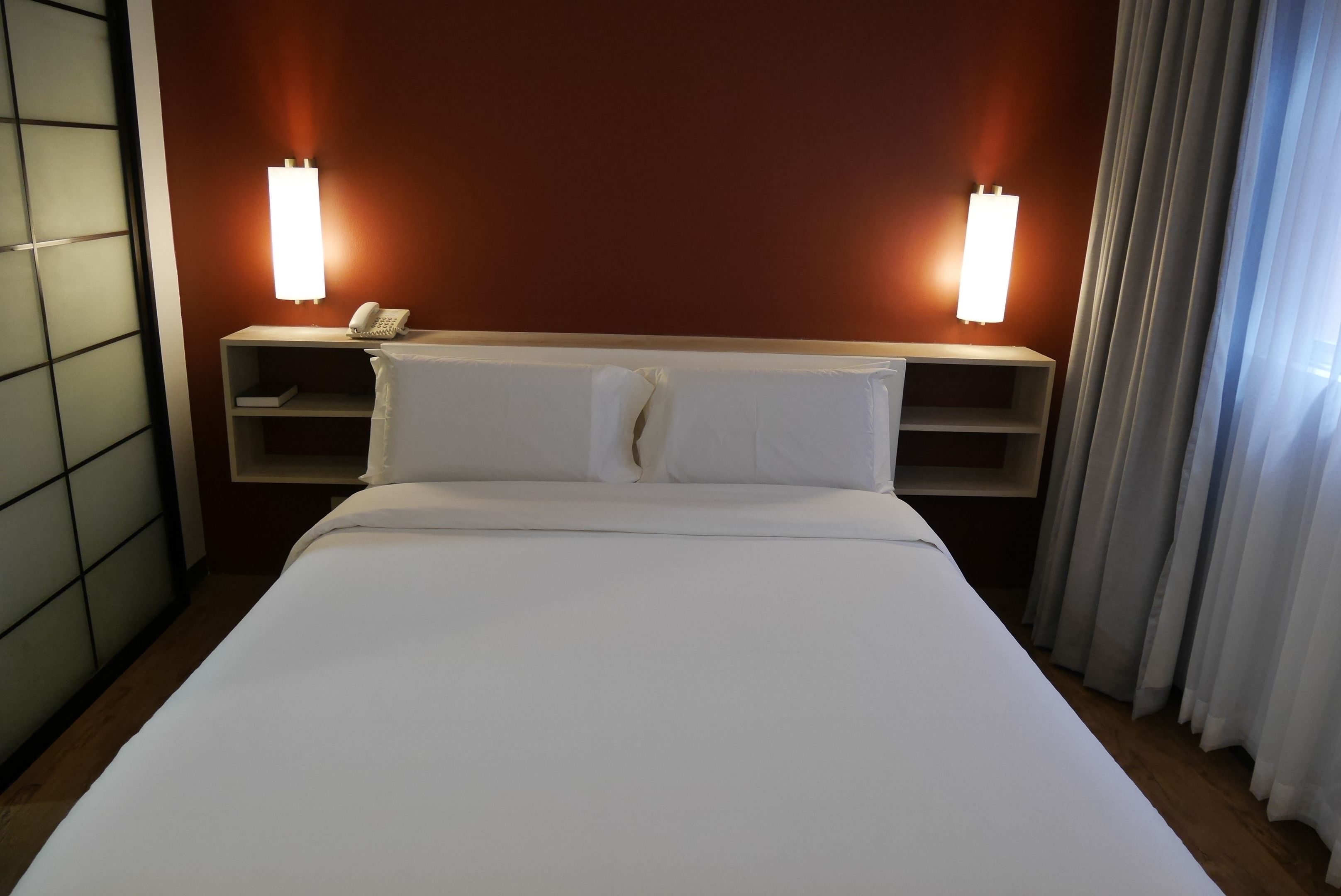 Et hotelværelse med en stor seng, to sengeborde med lamper, en telefon og et gardin.