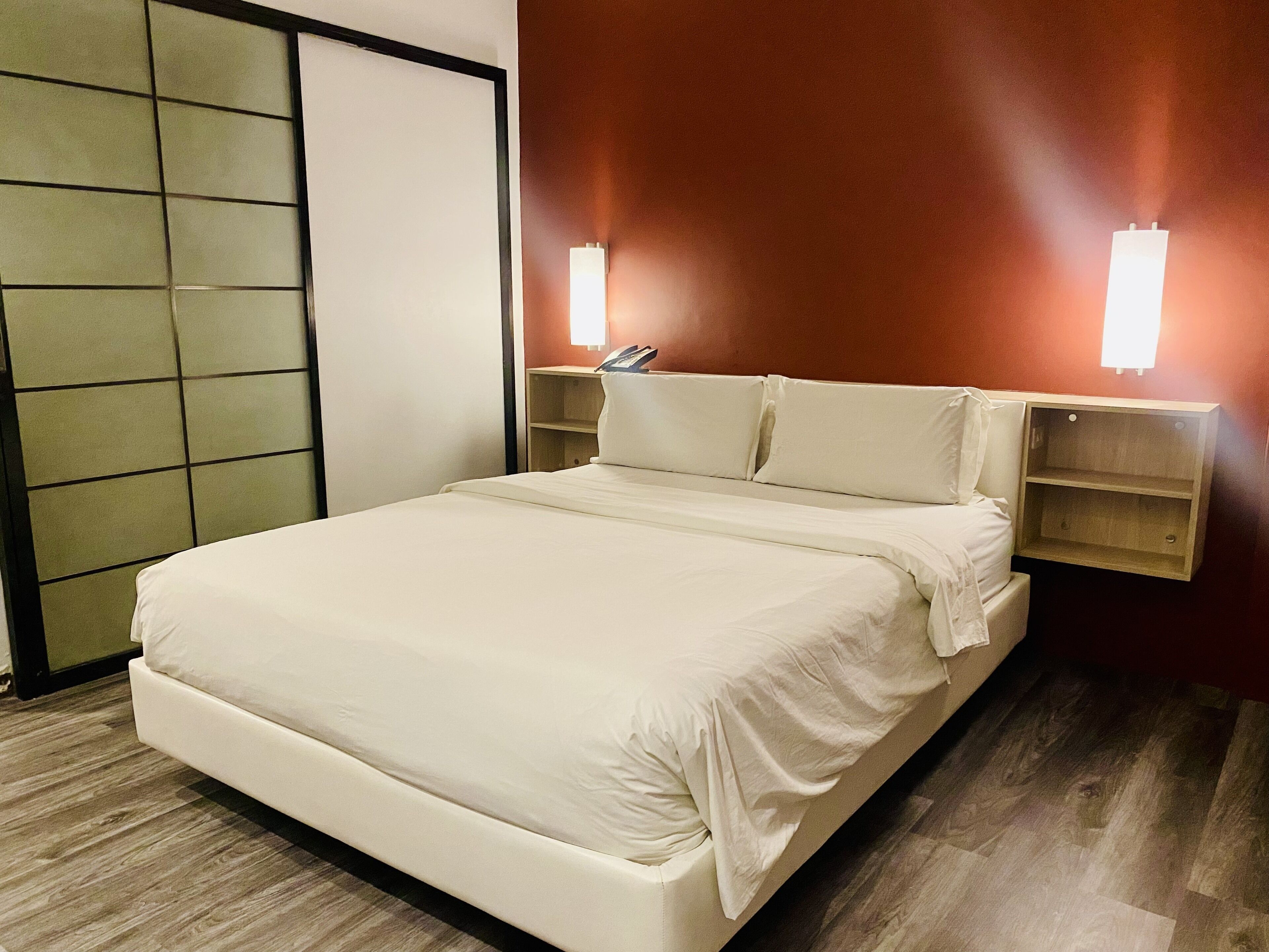 Ein ordentlich bezogenes Bett in einem Hotelzimmer mit Holzboden, einer Schiebetür und zwei Nachttischen mit Lampen.
