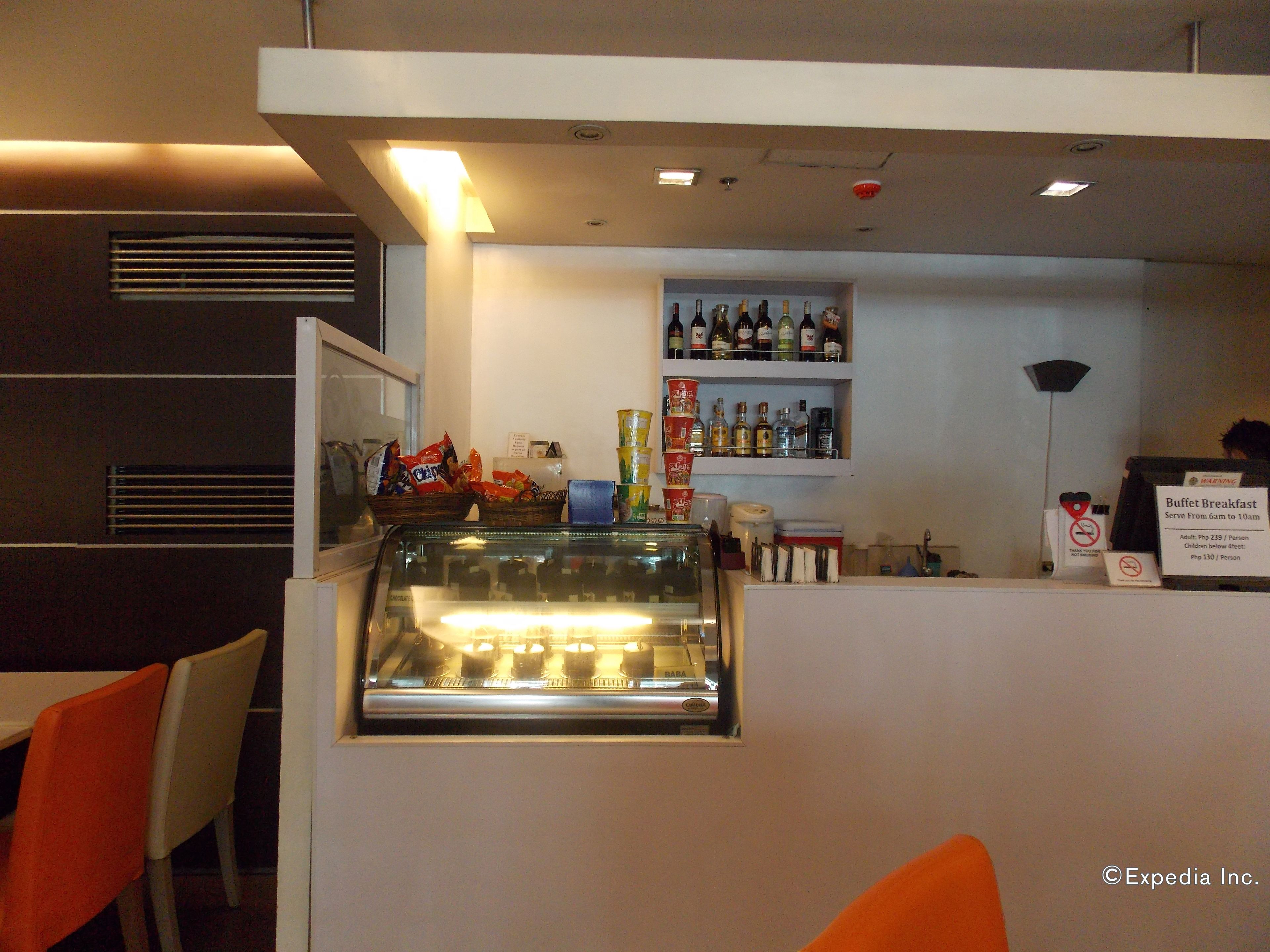 A buffet breakfast area with a glass display case, shelves with beverages, and a sign indicating the breakfast menu and prices.