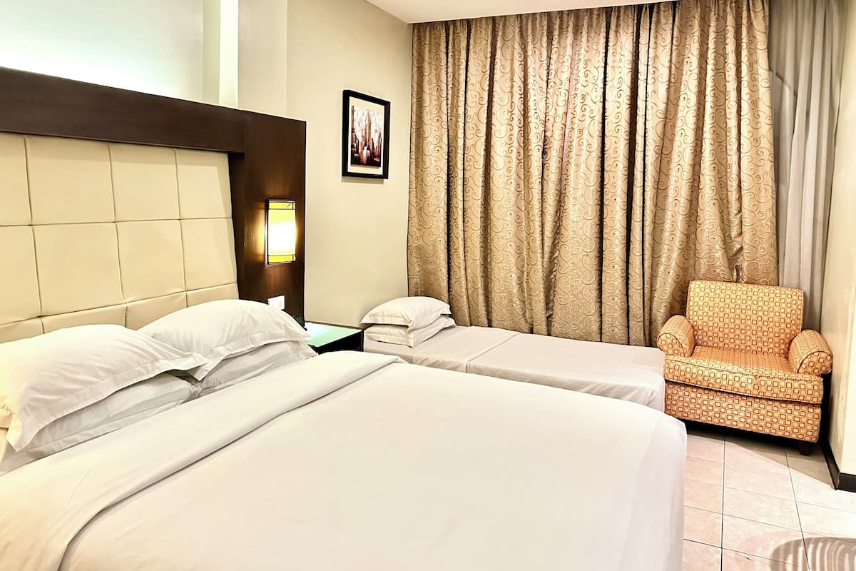 Quarto de hotel com duas camas, uma cadeira, uma mesinha de cabeceira e um quadro na parede.