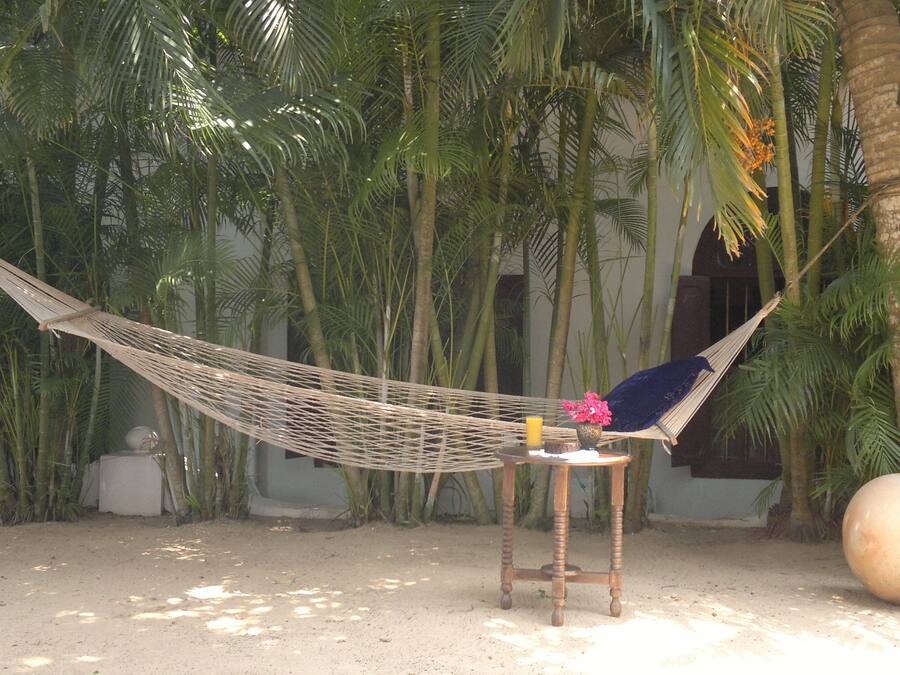 Una hamaca atada entre dos árboles en un jardín con una mesa redonda y una esfera decorativa grande cerca.