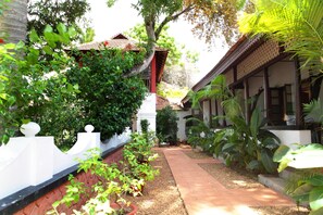 A courtyard with a pathway, surrounded by lush greenery and traditional architecture.