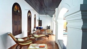 Un pasillo con puertas y arcos de madera, un banco y una mesa con un libro.