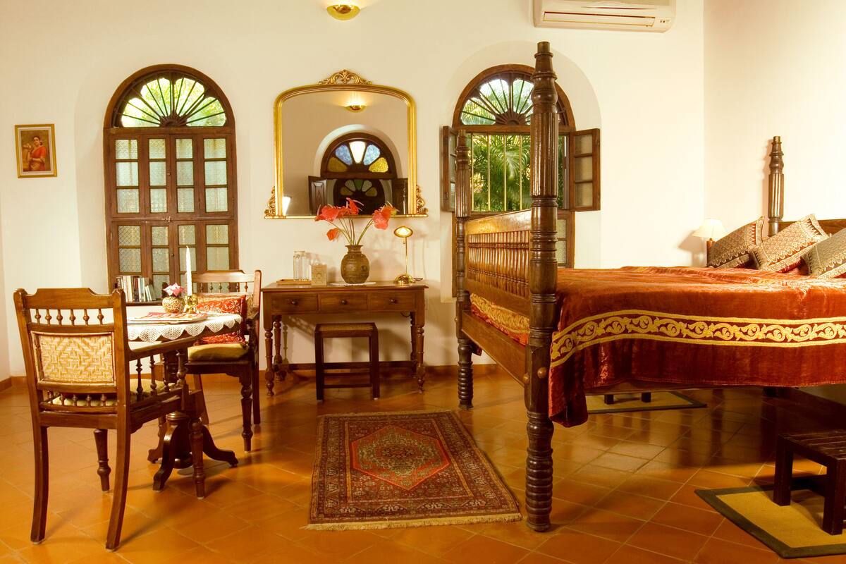 A traditional bedroom with a four-poster bed, a wooden desk with a chair, and a dining table with chairs.