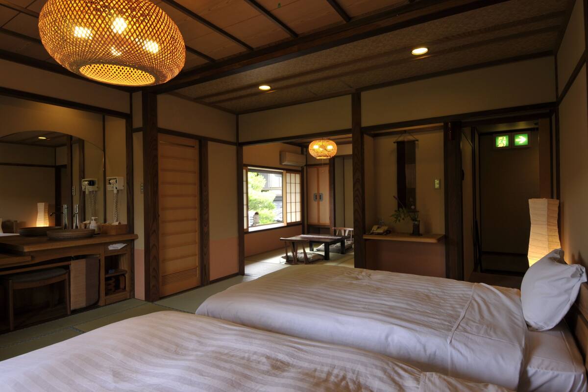 A traditional Japanese-style room with tatami flooring, a low wooden desk, a bed with white bedding, and a hanging lamp.