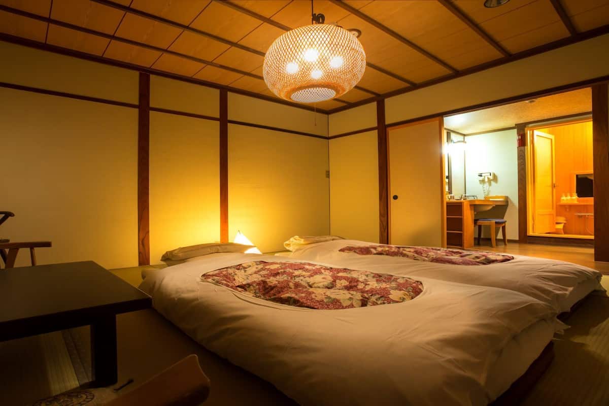 A traditional Japanese-style room with tatami flooring, a low wooden table, a bed with floral bedding, and a hanging paper lantern.