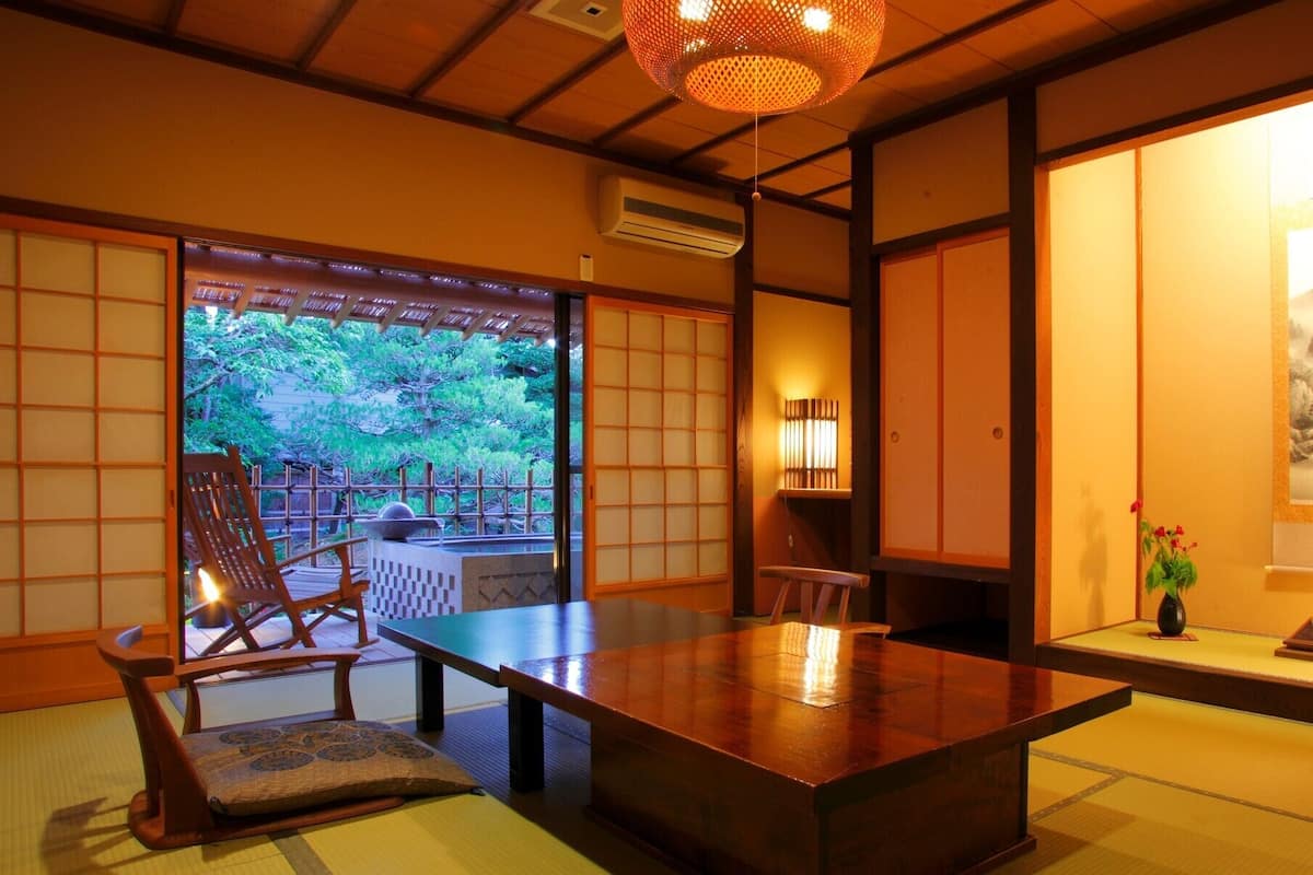A traditional Japanese room with tatami flooring, a low table, and a view of a garden.