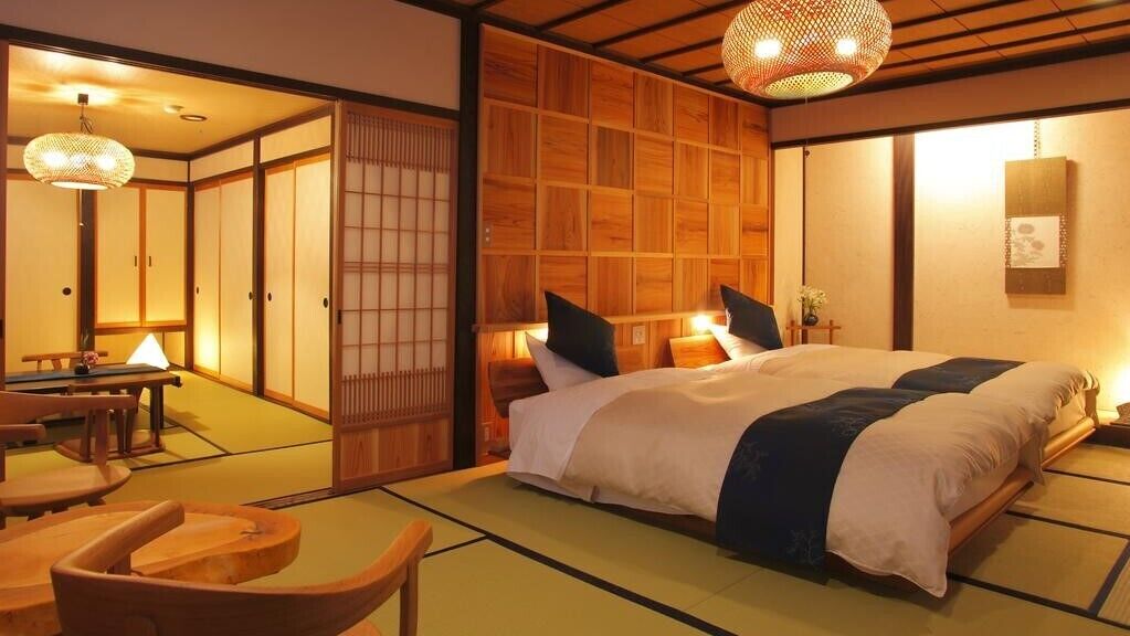 Ein traditionelles japanisches Schlafzimmer mit Tatami-Boden, einem großen Bett mit Kissen, einem Holzschrank und einer Schiebetür.