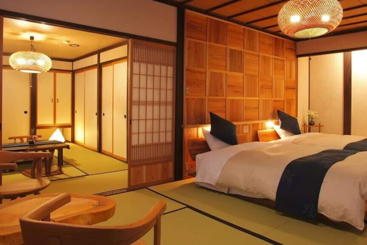 A traditional Japanese-style bedroom with tatami flooring, a large bed with pillows, a wooden wardrobe, and a sliding door.