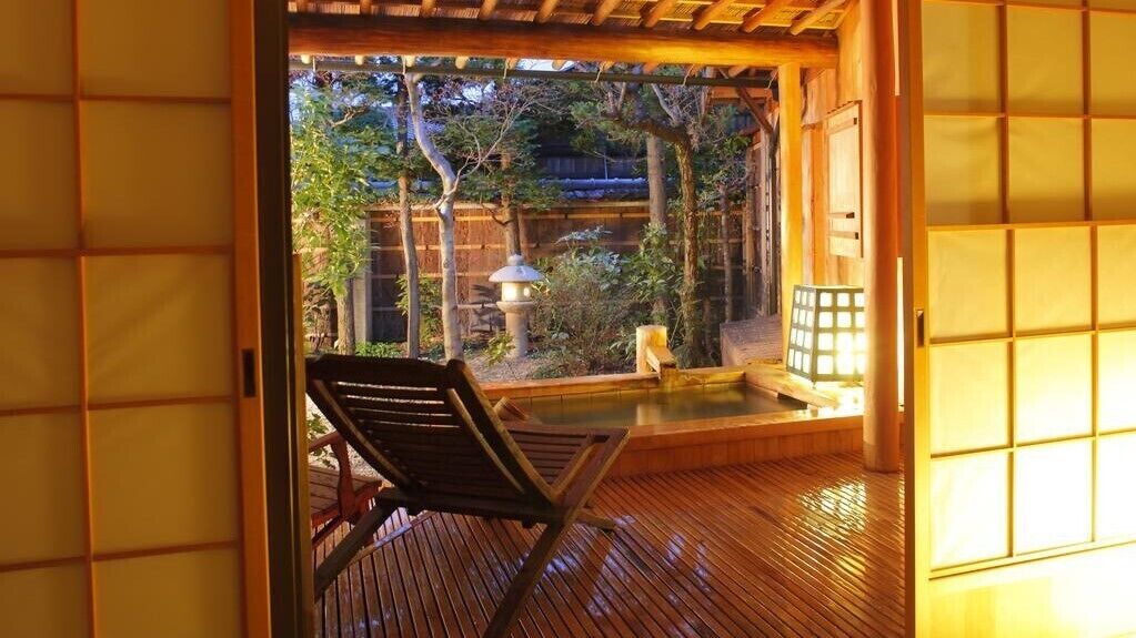 Ein traditioneller japanischer Raum mit Tatami-Böden, einem hölzernen Stuhl, einer kleinen Thermalbadewanne und Blick auf den Garten.