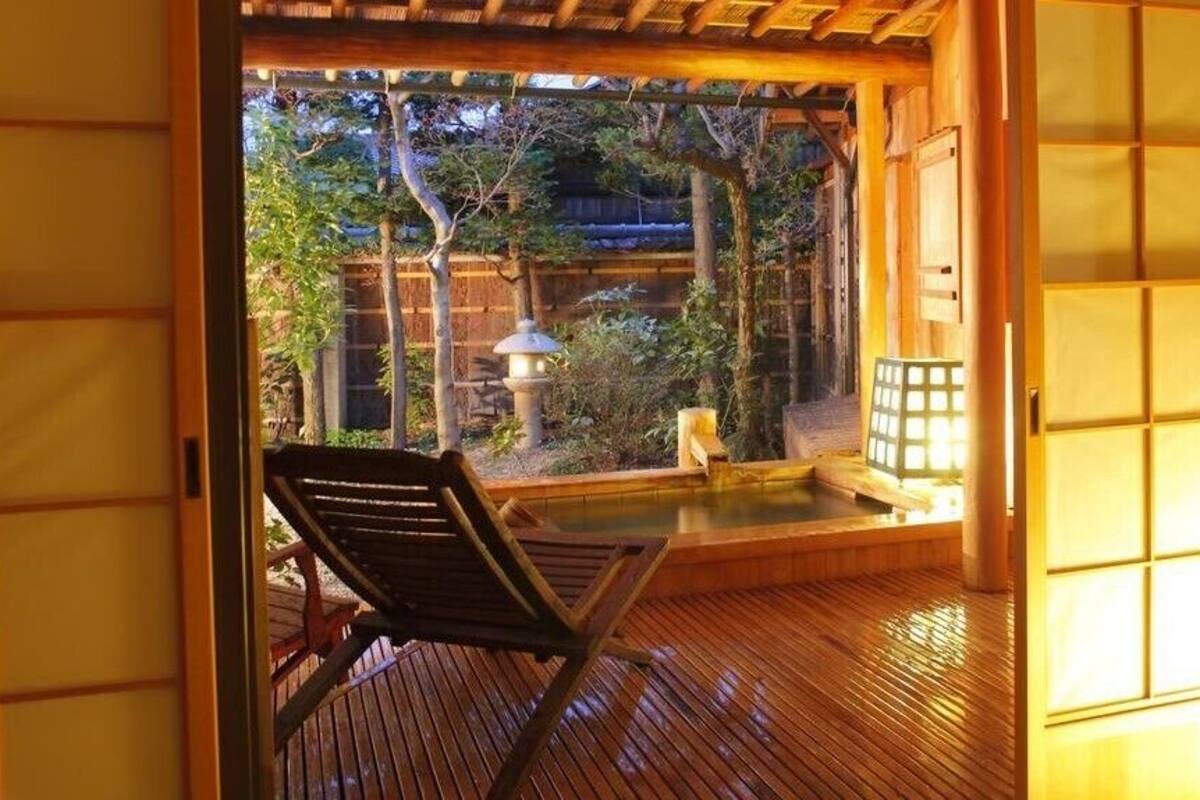 A traditional Japanese room with tatami flooring, a wooden chair, a small hot spring bath, and a view of the garden.