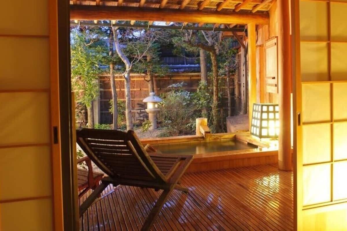 Quarto japonês tradicional com tatames, uma cadeira de madeira, uma pequena banheira termal e vista para o jardim.