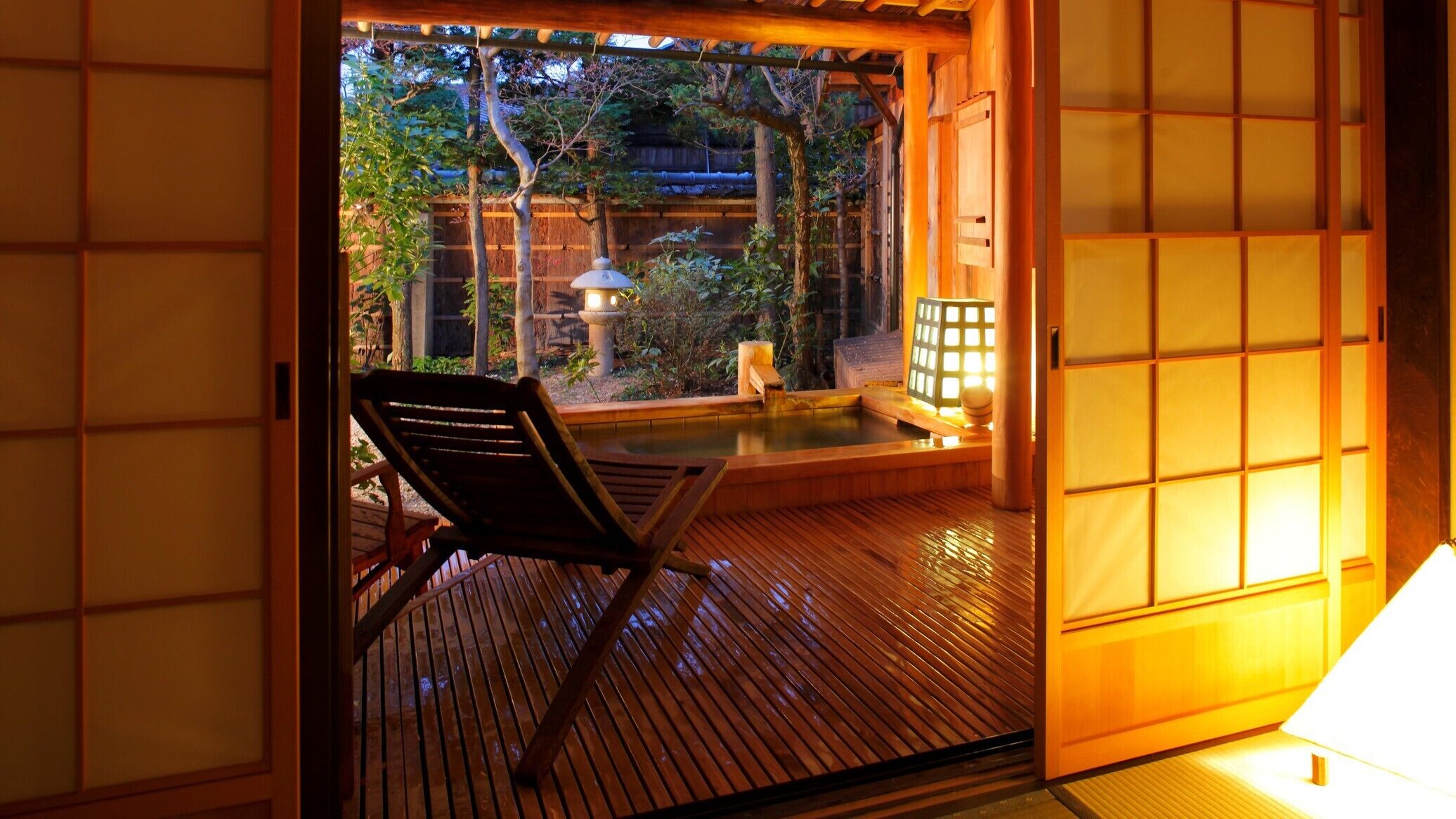 Ein traditioneller japanischer Raum mit Tatami-Boden, einem Holzstuhl und Blick auf einen Garten mit Wasserspiel.