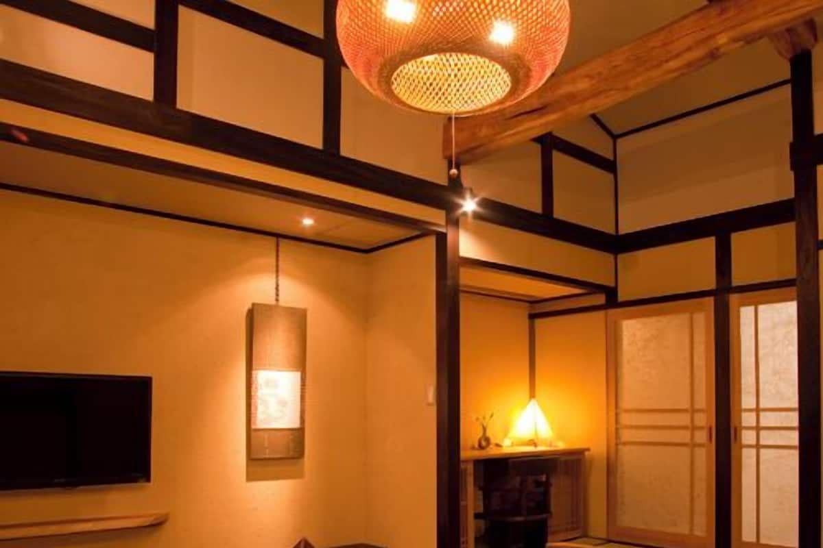 A traditional Japanese room with tatami flooring, a low table, wooden chairs, a television, and a hanging lamp.