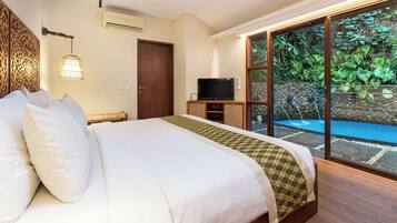 A hotel room with a large bed, a television on a wooden stand, and a view of a swimming pool and greenery outside.