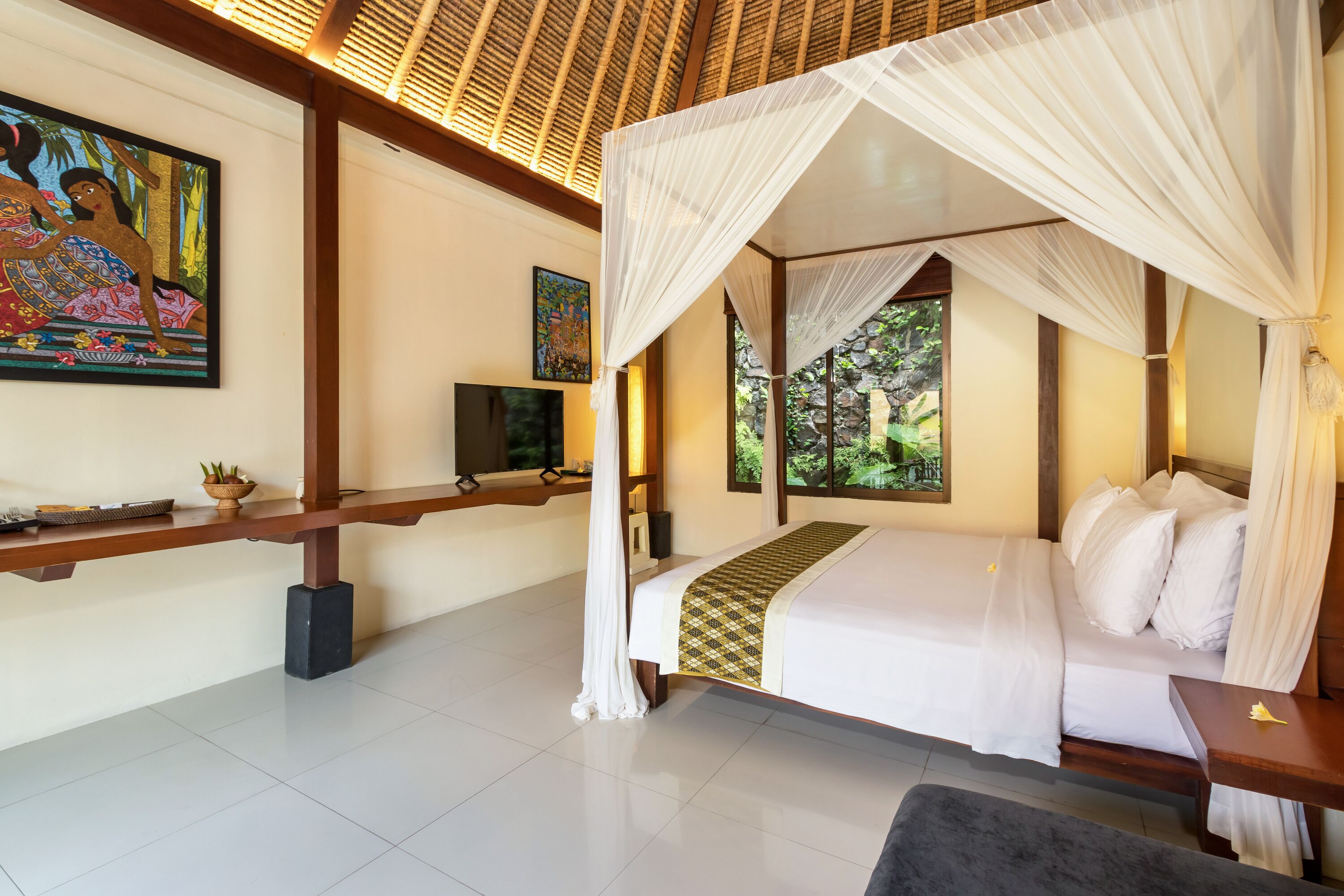 A bedroom with a four-poster bed, a television, and artwork on the walls.