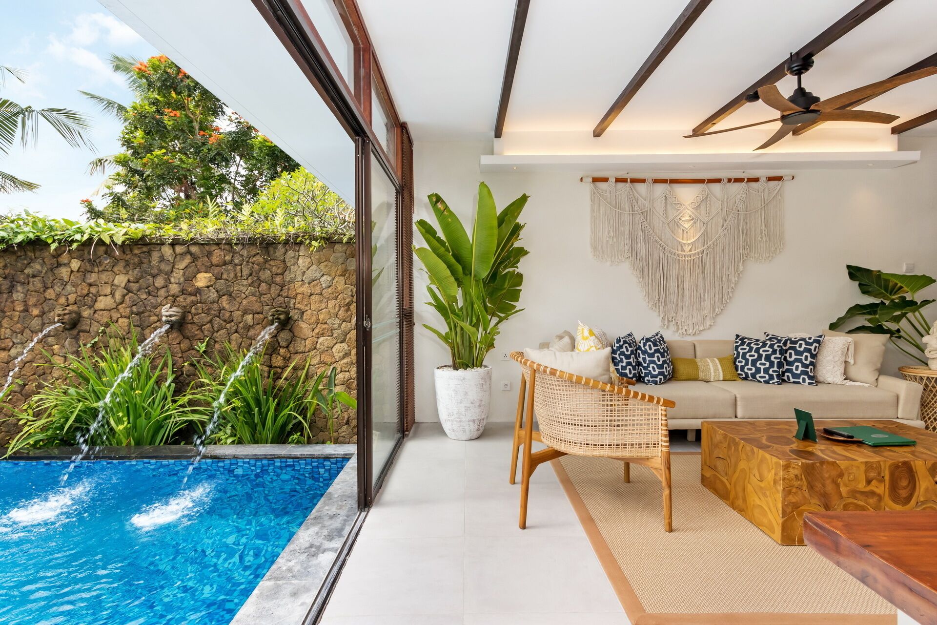Una sala de estar moderna con piscina, pared de piedra y plantas tropicales.