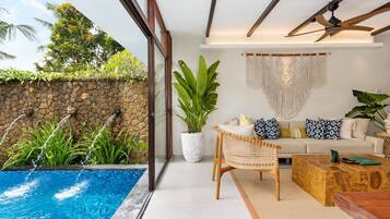 Una sala de estar moderna con piscina, pared de piedra y plantas tropicales.