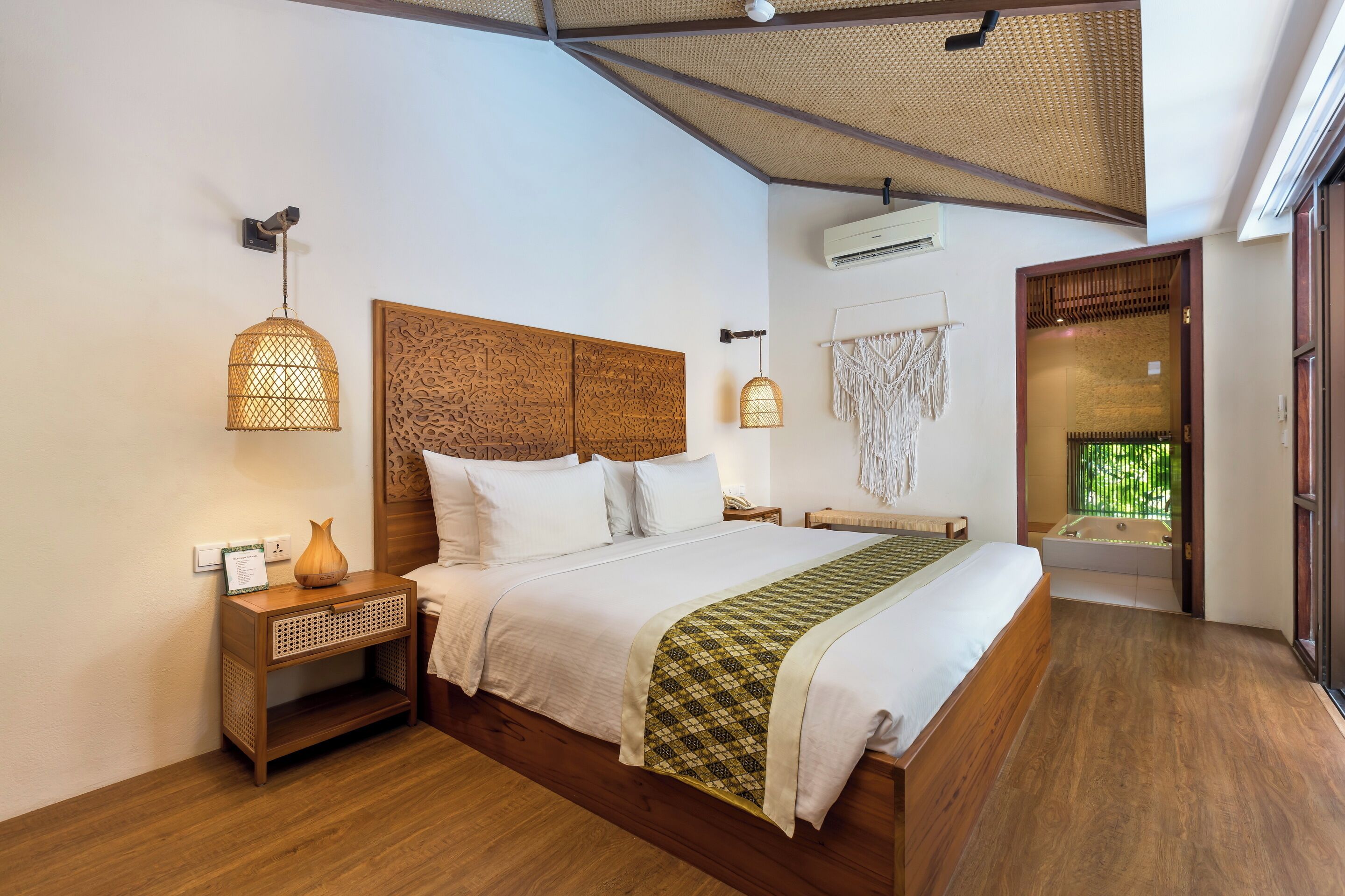 A bedroom with a large bed, a nightstand, a wall-mounted lamp, and a view of a bathroom with a bathtub.