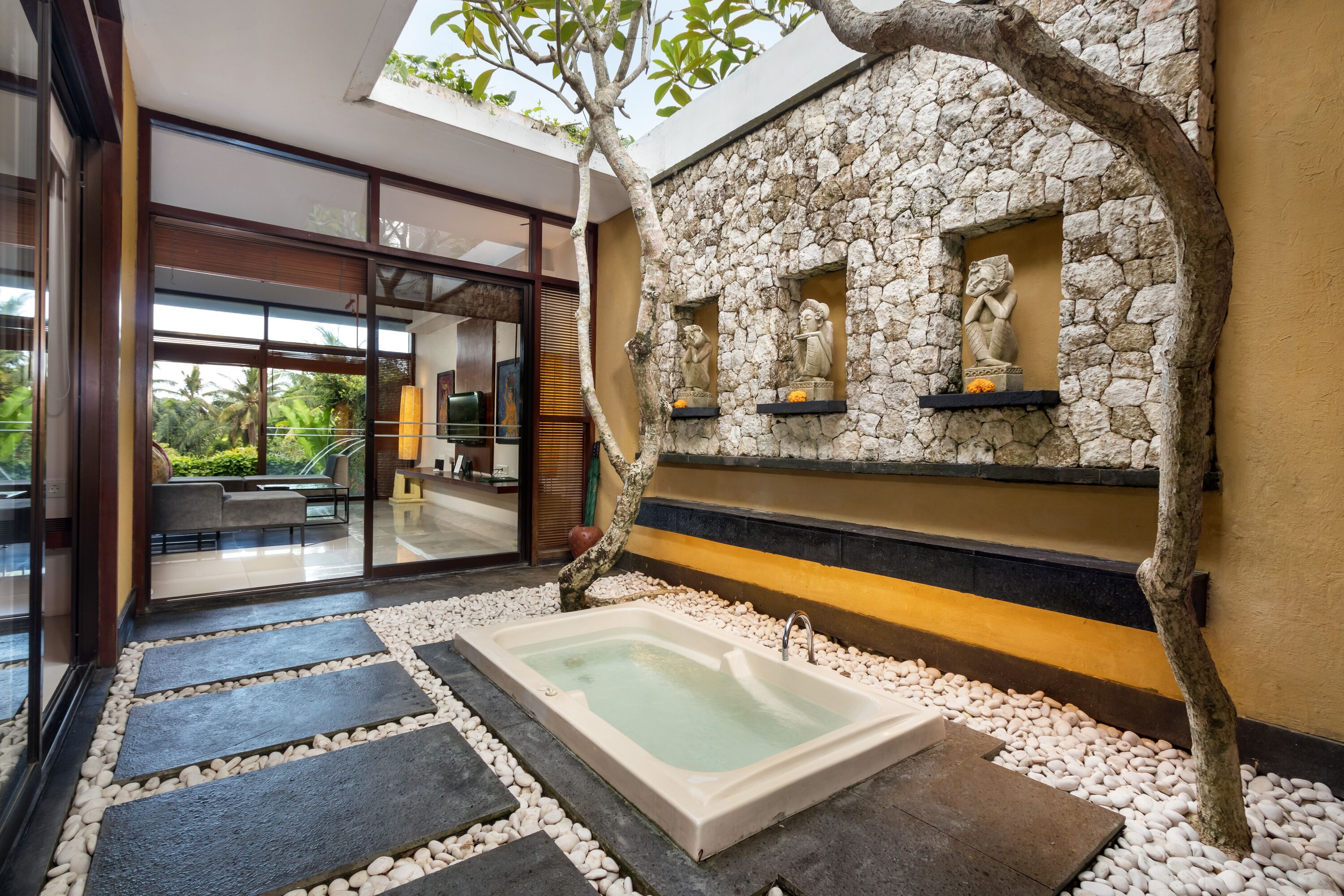 A spa area with a hot tub, stone wall with statues, and a glass door leading to a seating area.